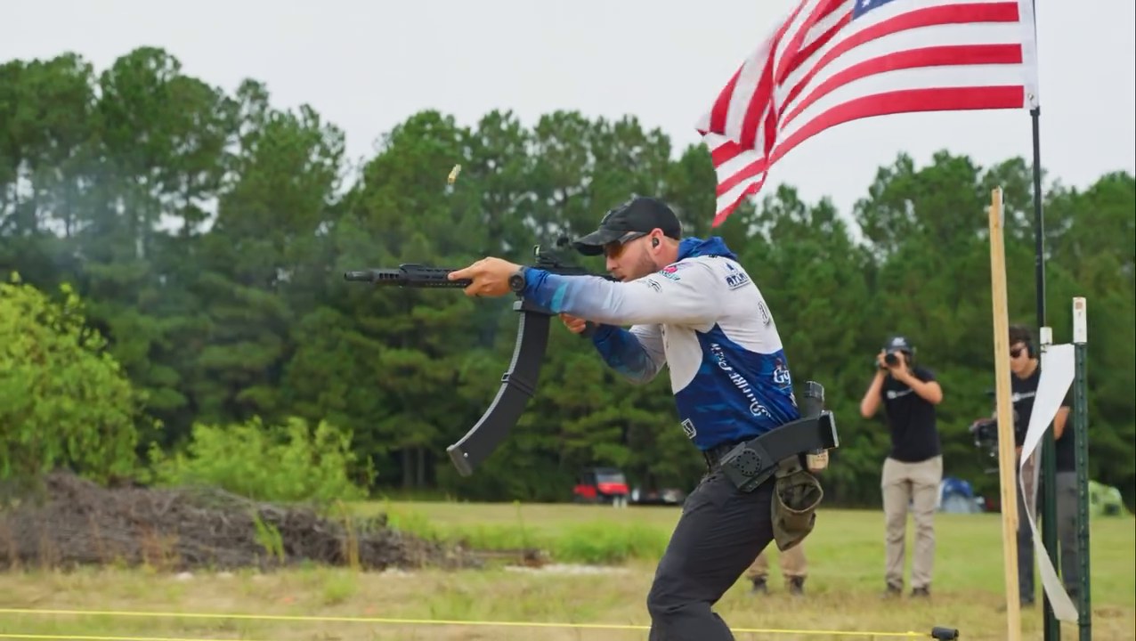 A competitor drives his rifle through a stage beneath the American flag