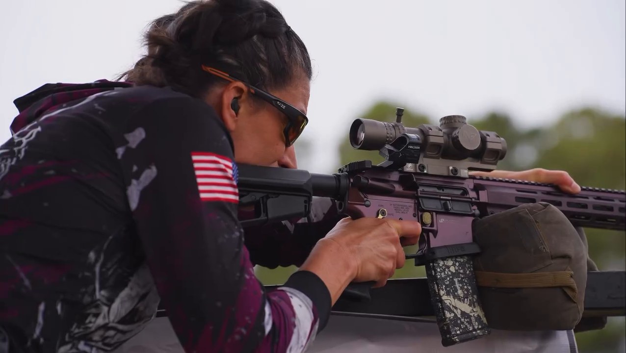A Memorial 3 Gun competitor sights in her rifle on a stage